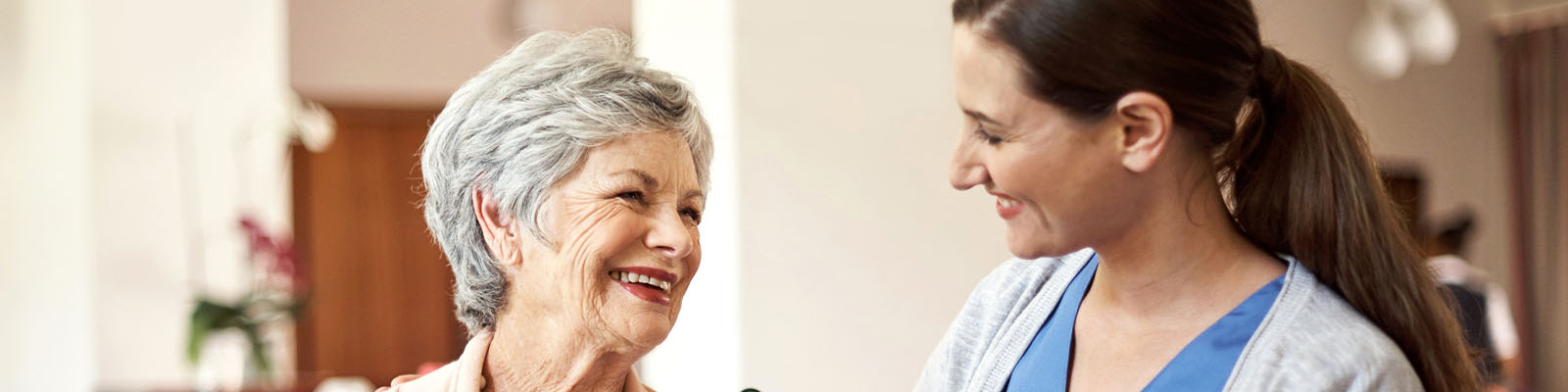 A senior woman in memory care looking over and smiling at nursing assistant