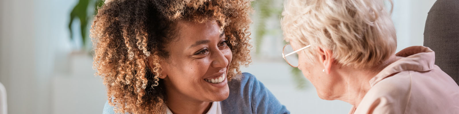 A senior woman wearing glasses looking at her nursing assistant and smiling